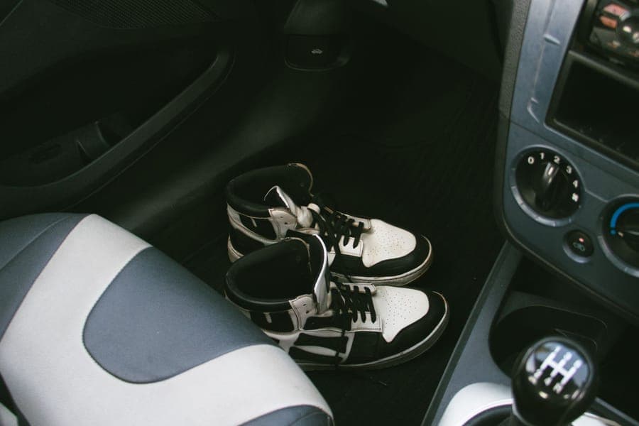 Driver footwell with sneakers resting on a dark rubber floor mat
