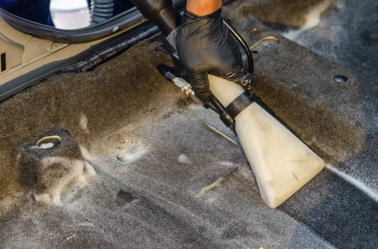 Gloved hand vacuuming grit out of a carpeted car floor